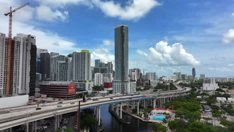 Aerial-rising-shot-of-downtown-Miami,-showcasing-modern-skyscrapers-and-elevated-highways-over-the-Miami-River