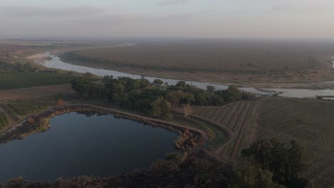 Push-forward-drone-view-of-seasonal-or-ephemeral-crocodile-river-by-sugarcane-farmlands-bordering-the-Kruger-National-Park