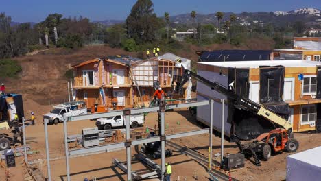 Aerial-low-push-in-shot-of-construction-crew-using-an-industrial-lift-crane-at-a-modular-housing-development-site-in-West-Los-Angeles,-California