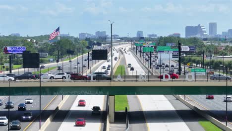 Busy-highway,-I-4-in-Orlando,-featuring-an-overpass-with-ORLANDO,-numerous-vehicles,-billboards,-and-a-distant-city-skyline