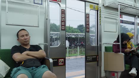 Passengers-in-a-commuter-train-in-Tangerang-Selatan,-one-sleeping-and-one-using-a-phone