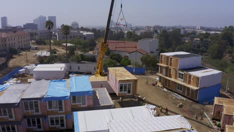 Aerial-descending-and-panning-shot-of-a-heavy-duty-lift-crane-lowering-a-housing-module-into-position-at-a-pre-fab-construction-site-in-West-Los-Angeles,-California