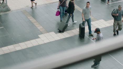 Busy-train-station-scene-with-passengers-walking-and-waiting,-viewed-from-an-overhead-perspective,-during-daylight