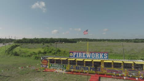 An-aerial-drone-view-of-a-fireworks-stand-with-a-large-inflatable-gorilla,-black-cat,-banners,-and-flags-on-the-4th-of-July-in-Houston,-Texas