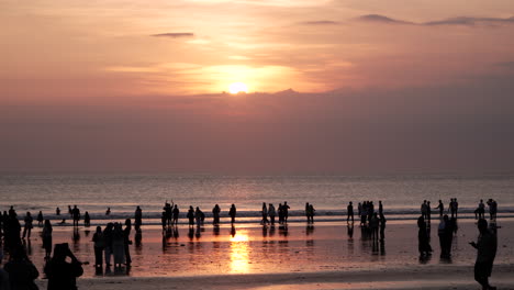 Silhouetted-Group-of-Tourists-Watching-Spectacular-Dramatic-Sunset-at-Seminyak-Beach-Seashore-in-Bali---wide-angle,-slow-motion,-copy-space