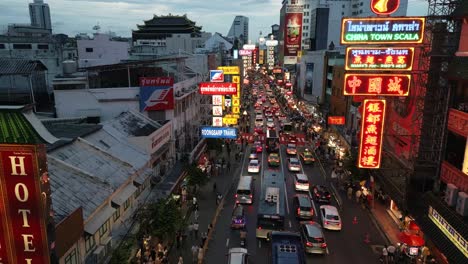 Drones-Vuelan-Sobre-La-Carretera-Yaowarat-En-Chinatown-Con-Vendedores-Ambulantes-De-Comida-Y-Tráfico-Por-La-Noche-Iluminados-Por-Letreros-De-Neón