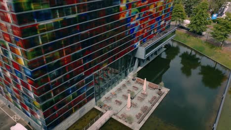 Footage-captures-an-aerial-descend-at-the-colorful-Beeld-en-Geluid-building-in-Media-Park-Hilversum,-showcasing-its-vibrant-glass-facade-and-modern-architecture