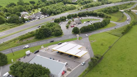 Drone-exterior-view-of-Shell-petrol-station-along-the-A30-in-Devon-UK,-surrounded-by-roads-and-greenery,-July-2024