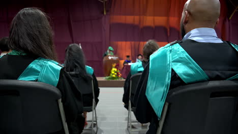 Toma-En-Cámara-Lenta-De-Estudiantes-Graduados-Con-Togas-Negras-Y-Capas-Turquesas-Escuchando-El-Discurso-Del-Director-De-La-Universidad-En-México