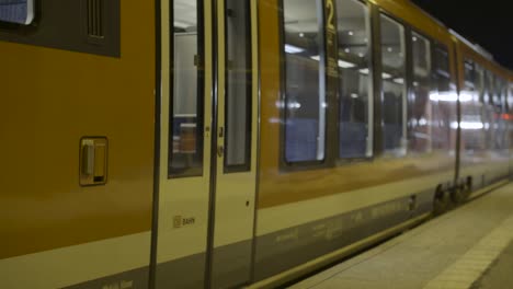 Deutsche-Bahn-train-leaves-a-snow-covered-platform-at-night,-lit-by-station-lights