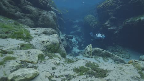 Underwater-view-of-diver-emerging-from-rocky-canyon-swimming-to-surface