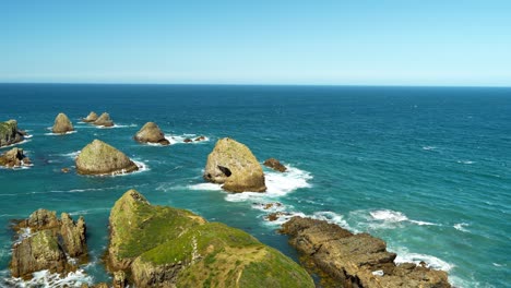 Aerial-panning-shot-of-mossy-rocks-and-boulder-at-coast-of-Nuggat-Point-in-Catlins,-New-Zealand