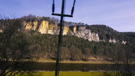 Train-window-view-of-the-river-and-cliffs-in-Elbe-Valley,-sustainable-travel-stable-copy-space,-czechia,-usti-nad-labem