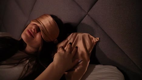 Stunning-young-female-model-resting-in-bed-at-night-wearing-a-sleeping-mask