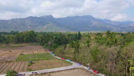 Aerial-view-of-a-convoy-of-colorful-VW-cars-running-on-the-path-of-beautiful-indonesia-rural-landscape