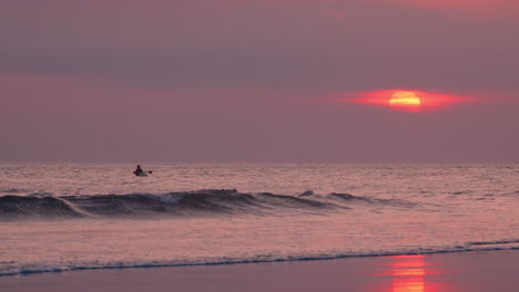 Silhouetted-Paddleboarder-Rawing-at-Sunset-With-Purple-Dramatic-Sky-on-Kuta-Beach,-Kuta-Beach,-Kuta,-Bali,-Indonesia