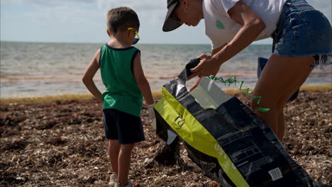 Cámara-Lenta-De-Un-Joven-Latino-Mexicano-Con-Gafas-De-Sol-Que-Se-Ofrece-Como-Voluntario-Para-Limpiar-La-Playa-En-México-Con-Su-Madre-En-Una-Mañana-Soleada