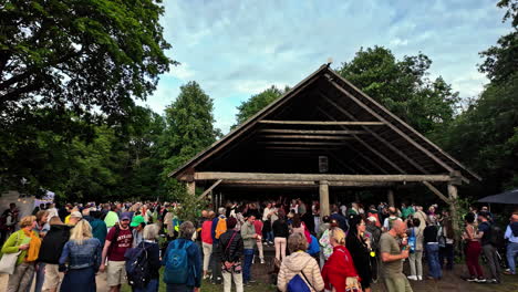 Large-crowd-of-people-handing-outside-under-open-air-covering-as-people-dance-in-hut