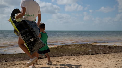 Slow-motion-of-a-mexican-latin-young-boy-wearing-shorts-holding-hands-with-his-mom-walking-towards-the-ocean-to-watch-the-sea-while-volunteering-to-clean-the-beach-in-Mexico