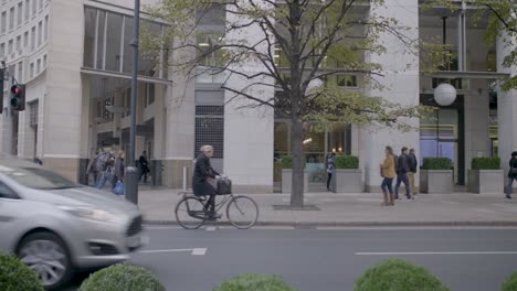 Blurred-black-cab-speeds-by-on-a-city-street-lined-with-modern-buildings-and-pedestrians