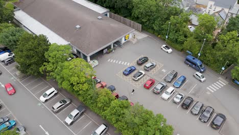 Drone-view-of-Lidl-supermarket-and-carpark-in-Okehampton,-Devon-UK,-July-2024,-showing-cars-and-surrounding-greenery