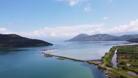 Aerial-view-of-the-serene-Albanian-landscape-near-Butrint-National-Archaeological-Park,-featuring-calm-blue-waters,-lush-greenery,-and-distant-mountains