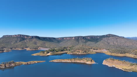 Perfect-sunny-day-flight-above-the-azure-waters-of-Cania-Dam,-towards-the-vast-cliff-topped-form-of-Castle-Mountain