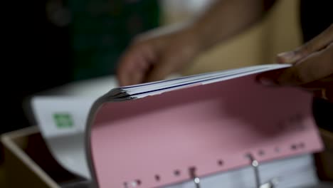 Close-up-of-hands-sorting-and-organizing-documents-in-a-pink-binder-folder,-depicting-office-work,-paperwork-management,-and-organization