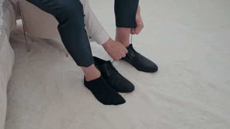 Man-sitting-down-and-tying-his-black-dress-shoes,-preparing-for-an-event