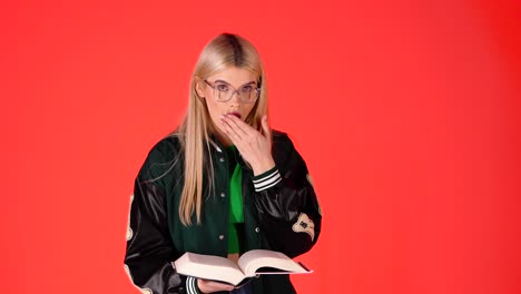 Una-Mujer-Rubia-Leyendo-Un-Libro-Y-Luego-Sorprendida-Y-Hace-Un-Gesto-Con-El-Pulgar-Hacia-Arriba,-Una-Colorida-Foto-De-Estudio