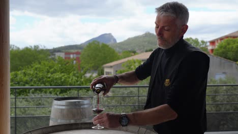 Man-pouring-red-wine-into-a-glass-outdoors-with-scenic-mountain-and-greenery-background