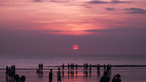 Crowd-of-People-at-Seminyak-Beach-Watching-Spectacular-Dramatic-Purple-Sunset-Over-Sea-in-Bali,-Indonesia---wide-angle,-slow-motion,-copy-space