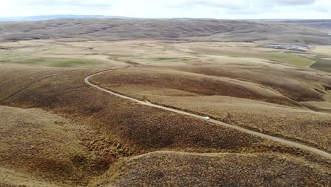 Un-Automóvil-Blanco-Conduce-Por-Un-Lago-Remoto-En-Una-Carretera-Lenta-En-El-Centro-De-Otago