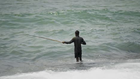 A-man-fishing-in-the-waves-of-the-Indian-Ocean-in-Sri-Lanka-on-a-calm-day-with-overcast-skies