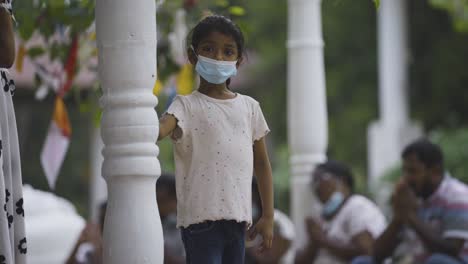 Young-girl-in-a-mask-looks-around-curiously-at-a-Sri-Lankan-temple