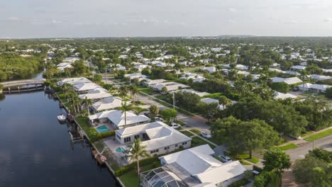 Vista-Aérea-De-Un-Exuberante-Barrio-Suburbano-Con-Casas-Con-Techos-Blancos,-Calles-Bordeadas-De-Palmeras-Y-Jardines-Verdes