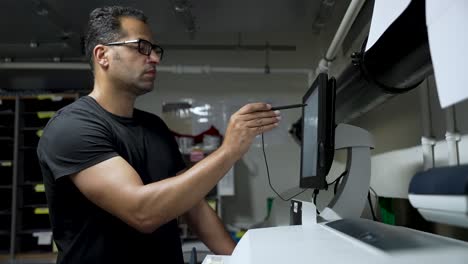 Un-Hombre-Con-Camisa-Negra-Interactúa-Con-Un-Dispositivo-De-Pantalla-Táctil-En-Un-Entorno-Industrial-O-Laboral,-Destacando-La-Tecnología-Moderna-Y-La-Interacción-Hombre-máquina