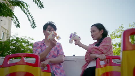 happy-asiatic-young-couple-play-together-with-toy-gun-while-travelling-on-ope-bus-visiting-new-holiday-summer-destination