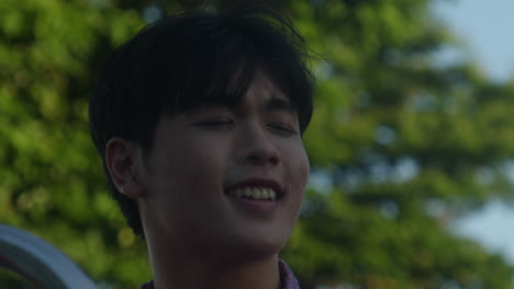 Close-up-asiatic-male-enjoying-the-sunshine-smiling-while-listening-to-music-with-cityscape-and-soap-bubble-on-background