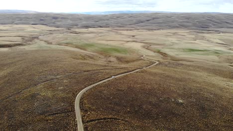 Un-Coche-Blanco-Conduce-Por-Un-Lago-Remoto-En-Una-Carretera-Lenta-En-El-Centro-De-Otago-Central