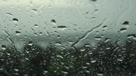 Closeup-raindrops-water-droplets-trickling-down-on-wet-clear-car-window-glass-during-heavy-rain-against-beach-view-in-rainy-day-monsoon-season