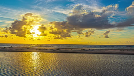 Ein-Zeitraffer-Fängt-Die-Atemberaubende-Schönheit-Eines-Sonnenuntergangs-über-Einer-Ruhigen-Lagune-Ein,-Während-Die-Sonne-Ihre-Goldenen-Strahlen-Auf-Das-Wasser-Und-Die-Wolken-Wirft