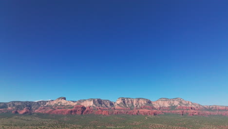 Drone-pulls-back-and-tilts-down-from-blue-sky-to-reveal-red-rock-mountains-and-desert-foreground-in-Sedona,-AZ