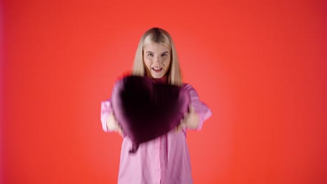 Hübsche-Blonde-Frau-Lächelt-Und-Hält-Einen-Lila-Herzförmigen-Ballon-Vor-Rotem-Hintergrund,-Studioaufnahme