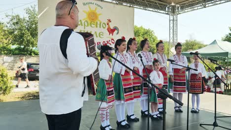 Las-Niñas-Del-Coro-Folclórico-Búlgaro-Cantan-En-El-Festival-De-Verano-Al-Músico-De-Acordeón