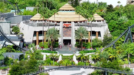 Jurassic-Park-attraction-at-Universal-Studios-Orlando,-featuring-lush-tropical-greenery,-roller-coaster,-and-the-iconic-entrance-building,-capturing-the-theme-park’s-vibrant-atmosphere