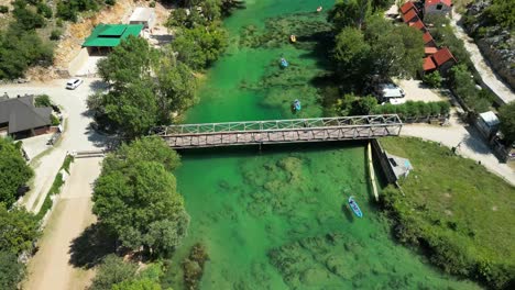 Bridge-over-green,-clean-river-Zrmanja-near-Zadar-and-kayaks-going-down-stream-with-camp-sites-both-side