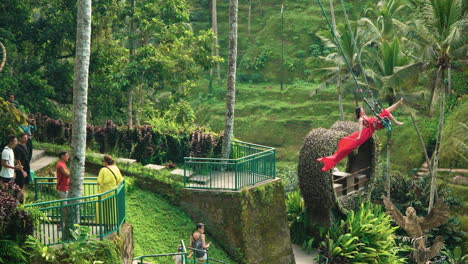 Frau-Im-Roten-Kleid-Auf-Bali-Swing-Mit-Reisenden,-Die-Die-Gegend-Erkunden-Und-Fotos-Machen