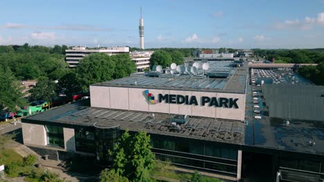 Drone-footage-captures-the-main-entrance-of-the-TV-studio-complex-at-Media-Park-in-Hilversum,-Netherlands,-showcasing-its-modern-architectural-design-and-bustling-activity