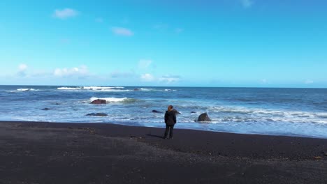 Blonde-Frau-Starrt-Allein-Auf-Das-Meer-Am-Vulkanischen-Strand-Von-Sao-Miguel-Auf-Den-Azoren,-Drohnen-Luftaufnahme